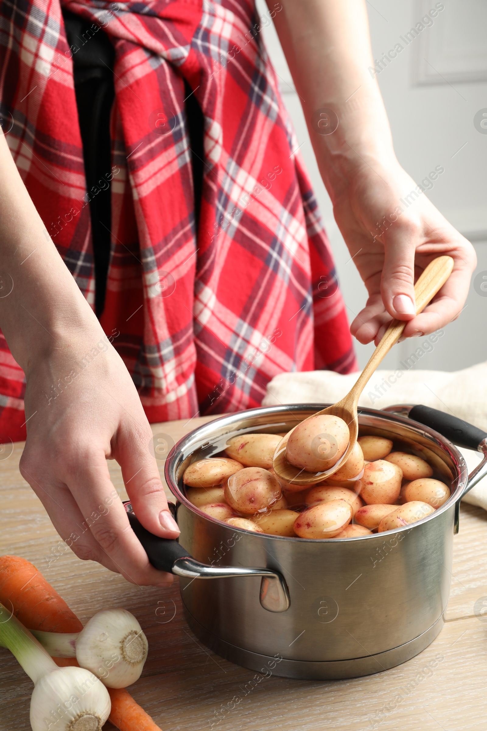 Photo of Woman taking raw potato from pot with water at wooden table, closeup