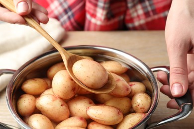 Photo of Woman taking raw potato from pot with water at table, closeup