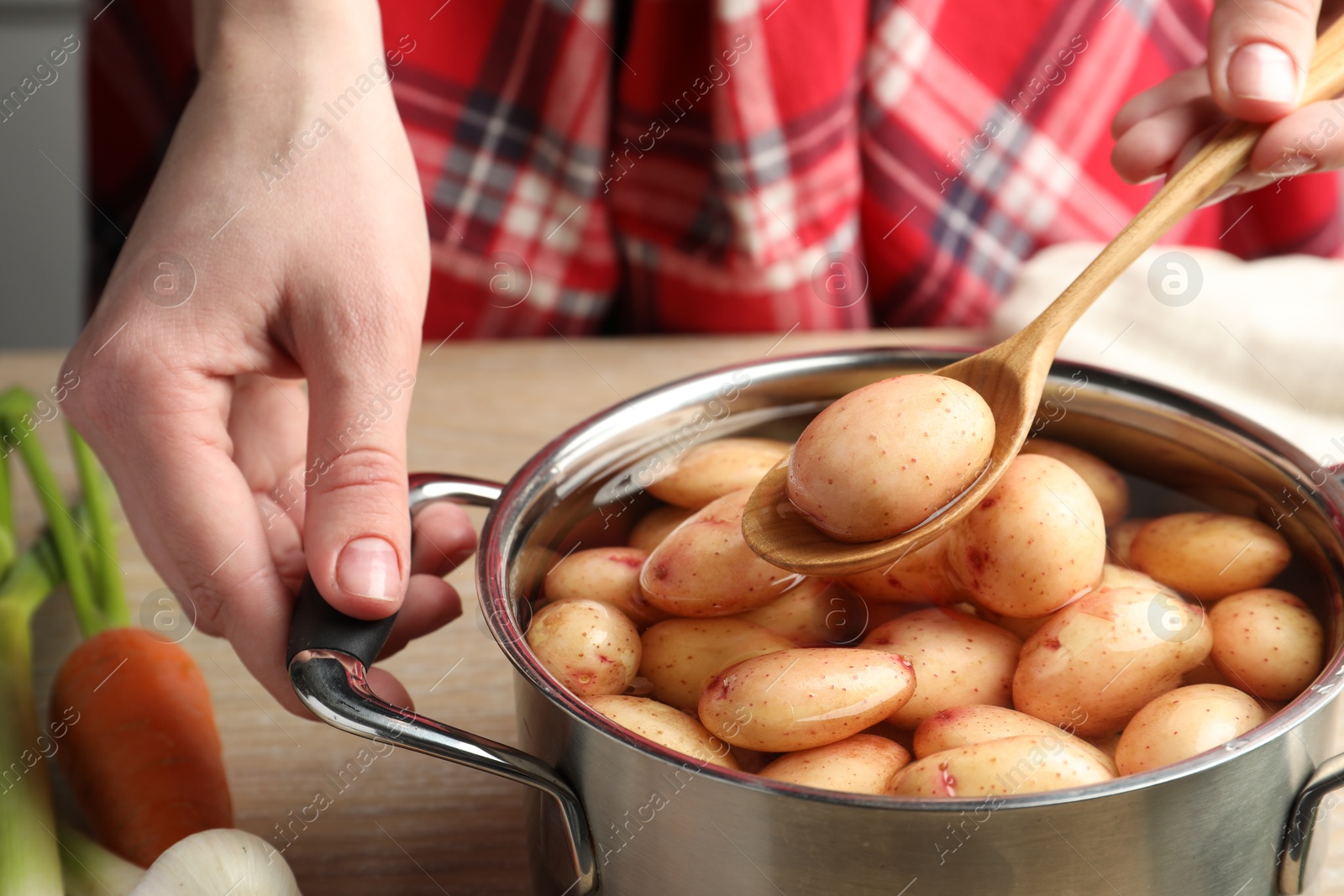 Photo of Woman taking raw potato from pot with water at table, closeup