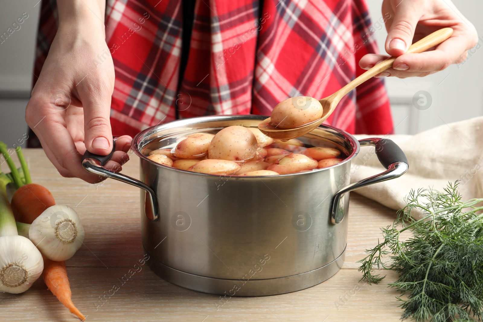 Photo of Woman taking raw potato from pot with water at table, closeup