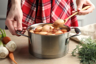 Woman taking raw potato from pot with water at table, closeup