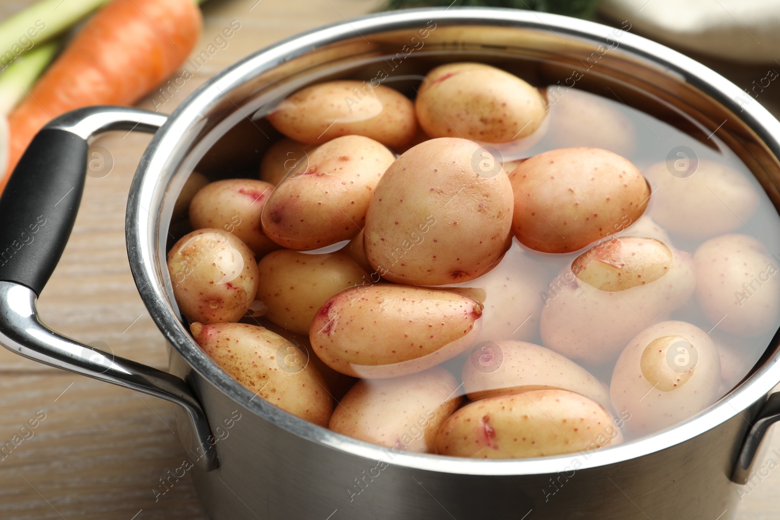 Photo of Raw potatoes in pot on wooden table, closeup