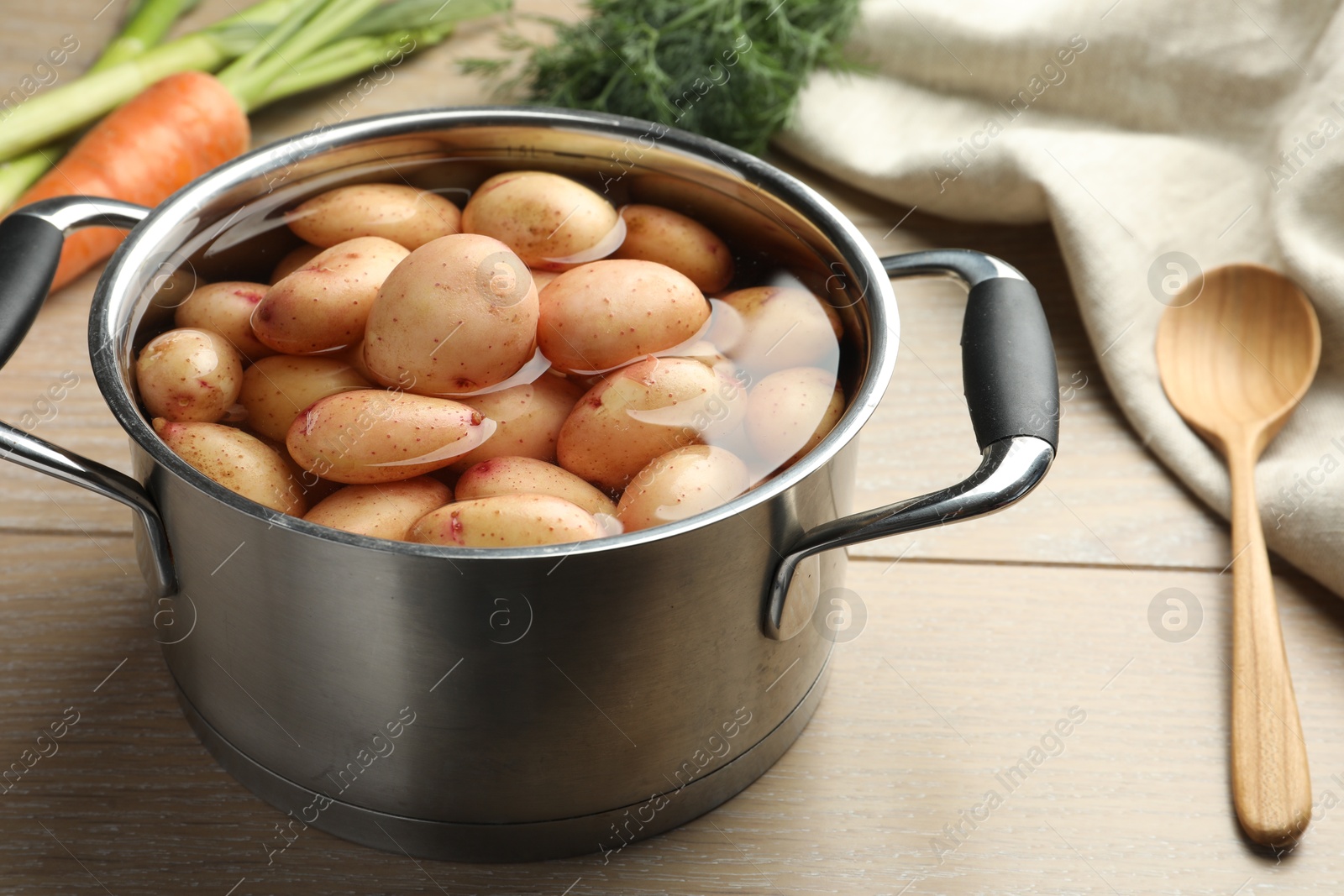 Photo of Raw potatoes in pot, carrot, dill and spoon on wooden table