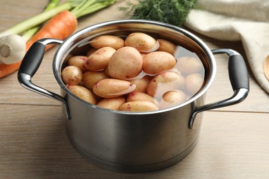 Raw potatoes in pot, green onion, carrot and dill on wooden table