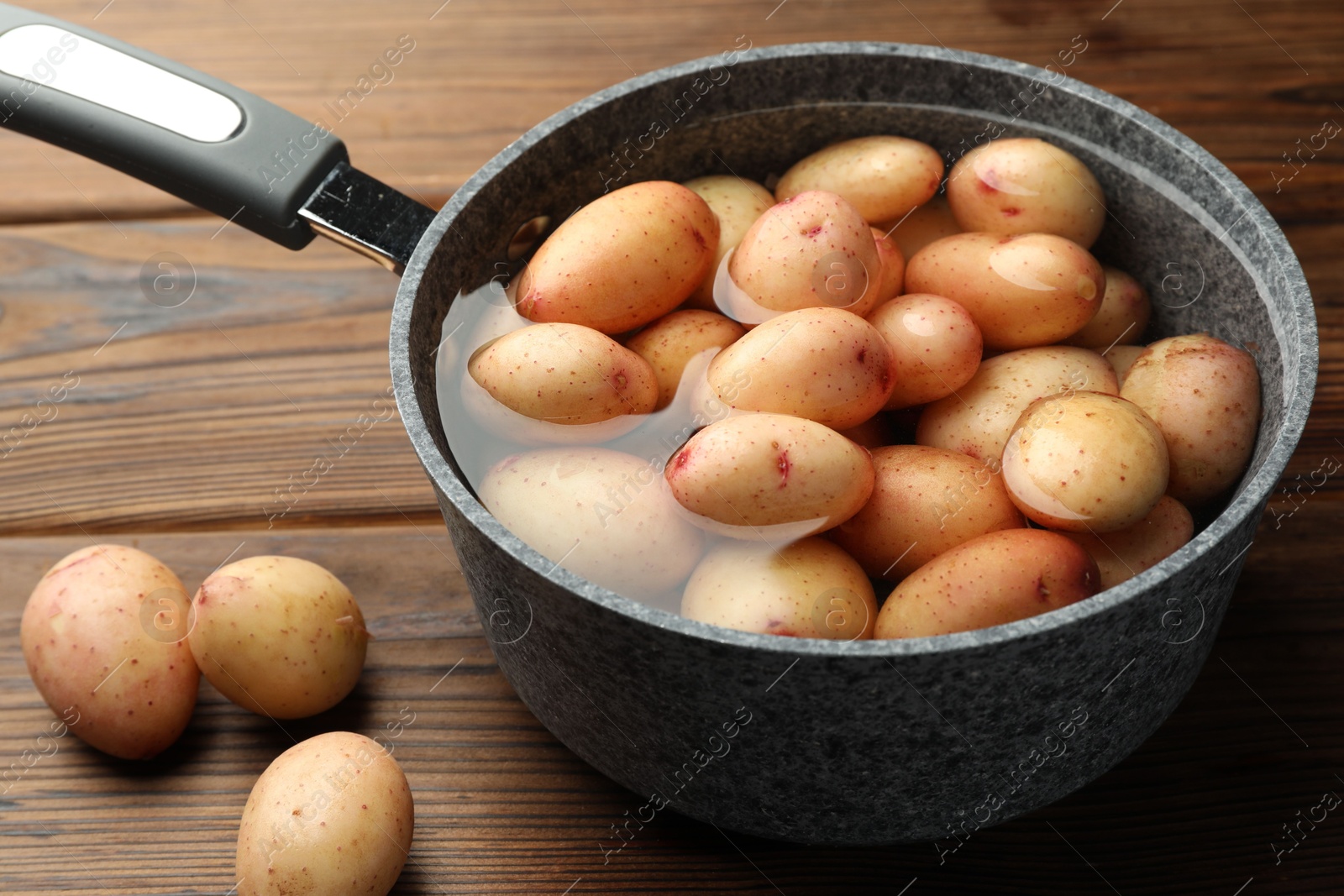 Photo of Raw potatoes in saucepan with water on wooden table