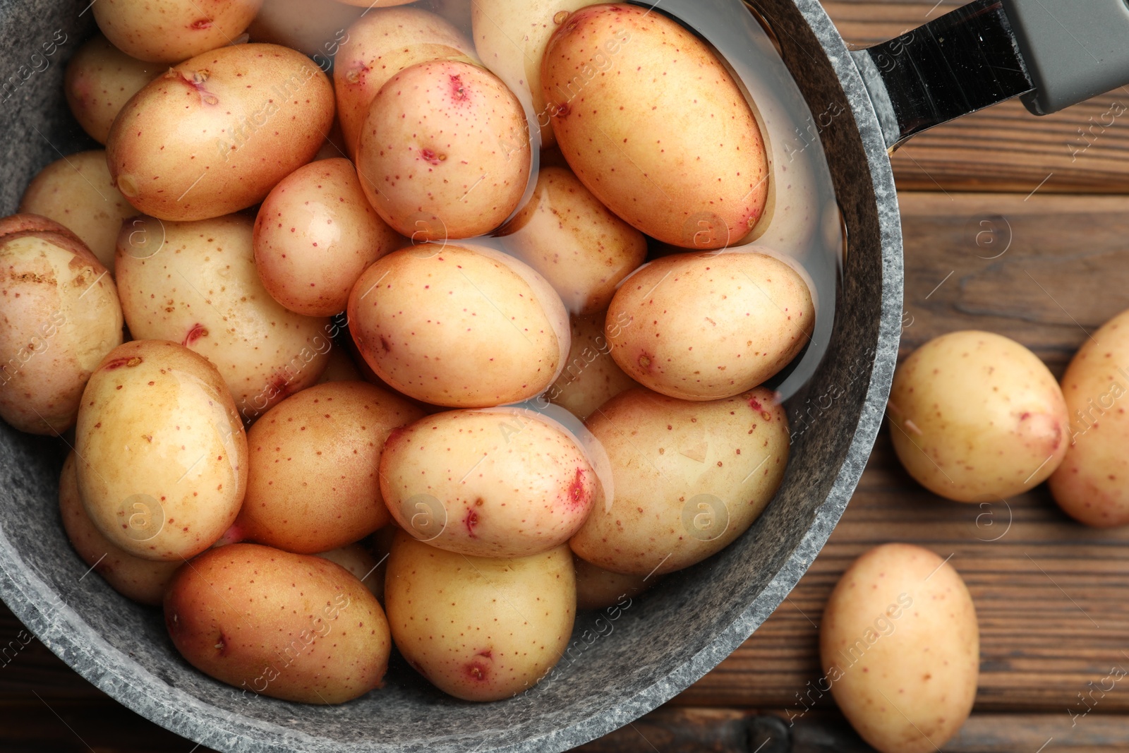 Photo of Raw potatoes in saucepan with water on wooden table, top view