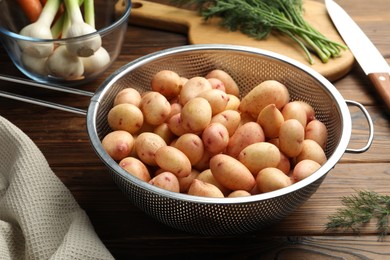 Raw potatoes in colander, dill, green onion and knife on wooden table