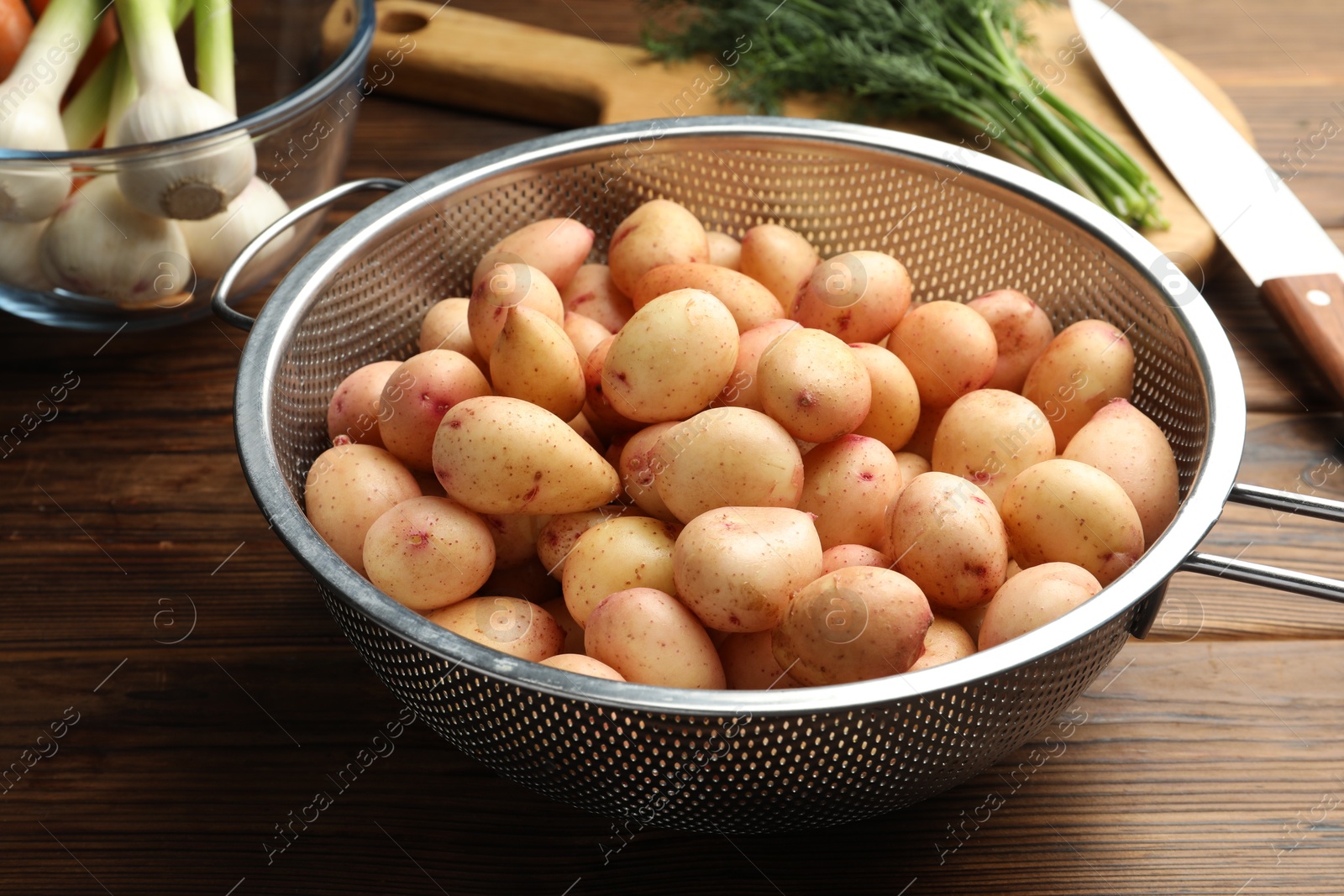 Photo of Raw potatoes in colander, green onion and knife on wooden table