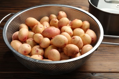 Photo of Raw potatoes in colander on wooden table, closeup