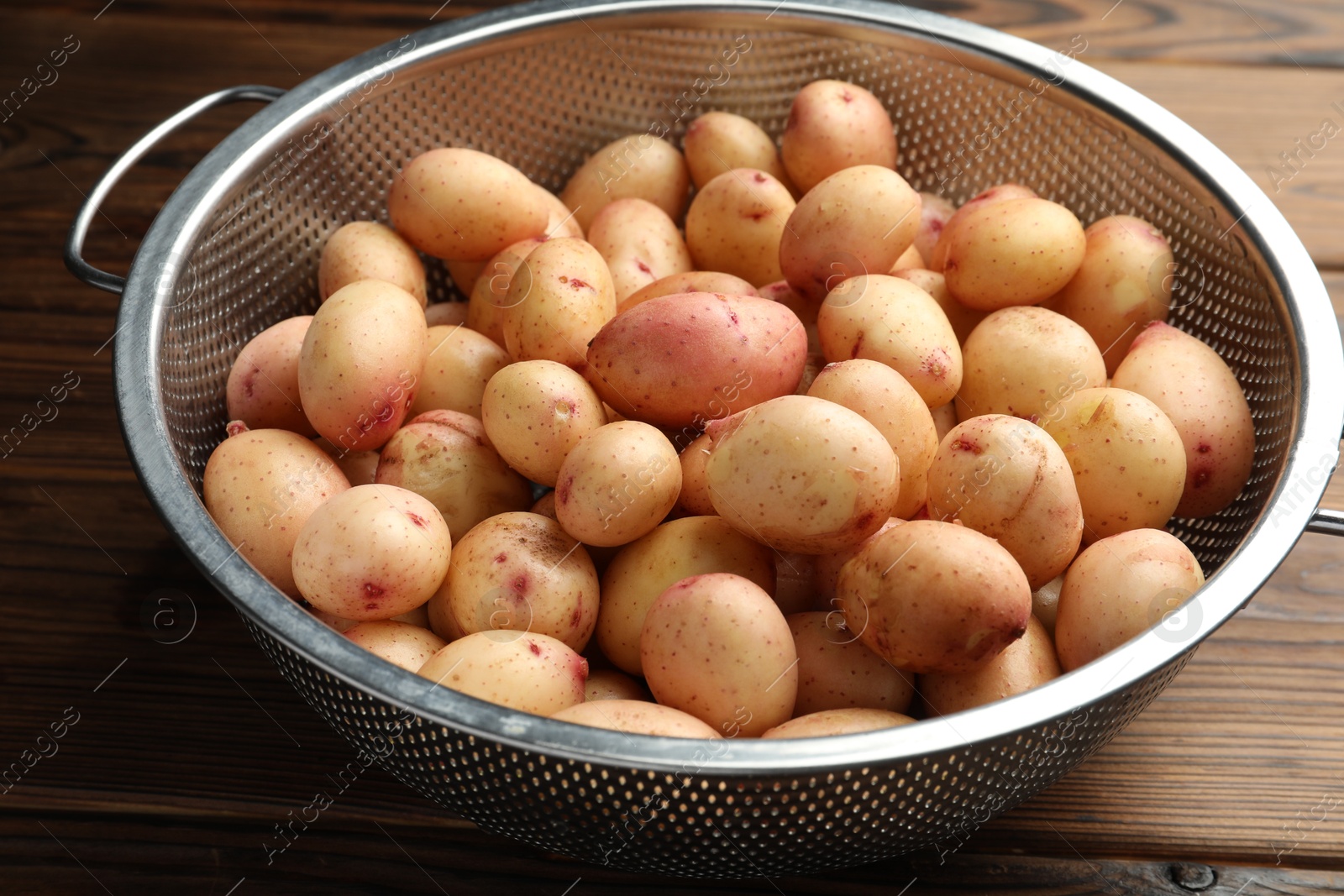 Photo of Raw potatoes in colander on wooden table, closeup