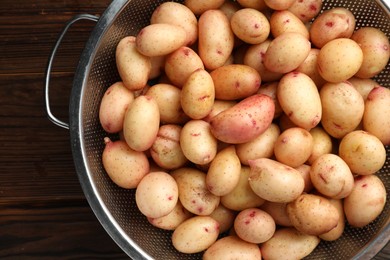 Photo of Raw potatoes in colander on wooden table, top view