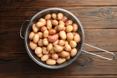 Photo of Raw potatoes in colander on wooden table, top view