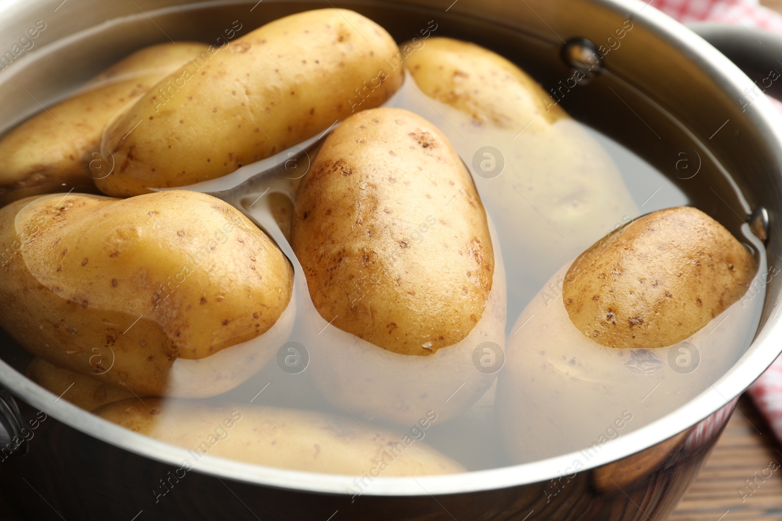 Photo of Raw potatoes in pot with water on table, closeup