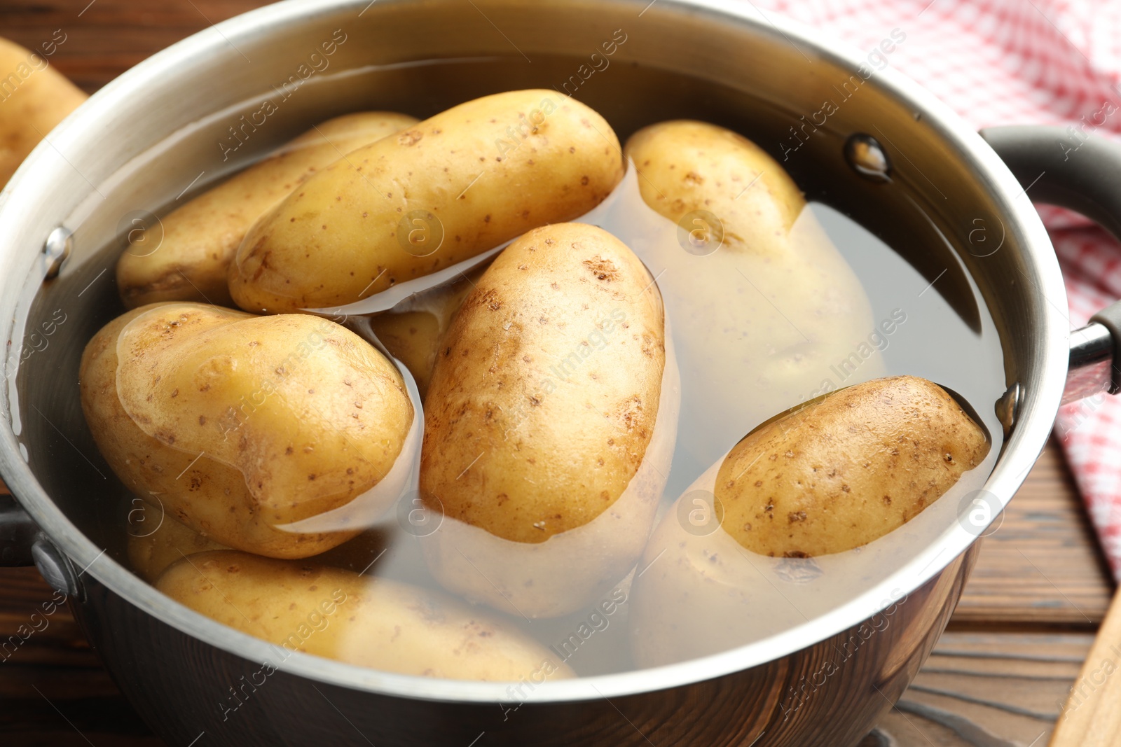 Photo of Raw potatoes in pot with water on wooden table, closeup