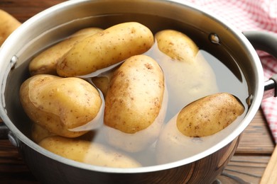 Raw potatoes in pot with water on wooden table, closeup