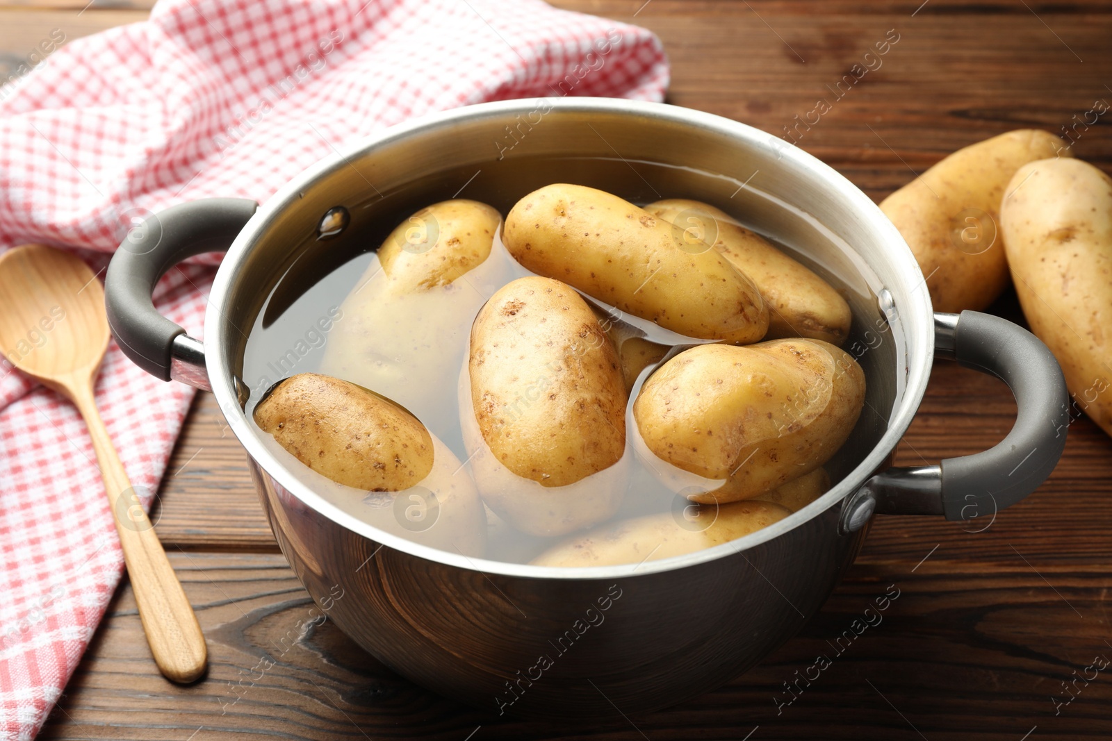 Photo of Raw potatoes in pot with water on wooden table