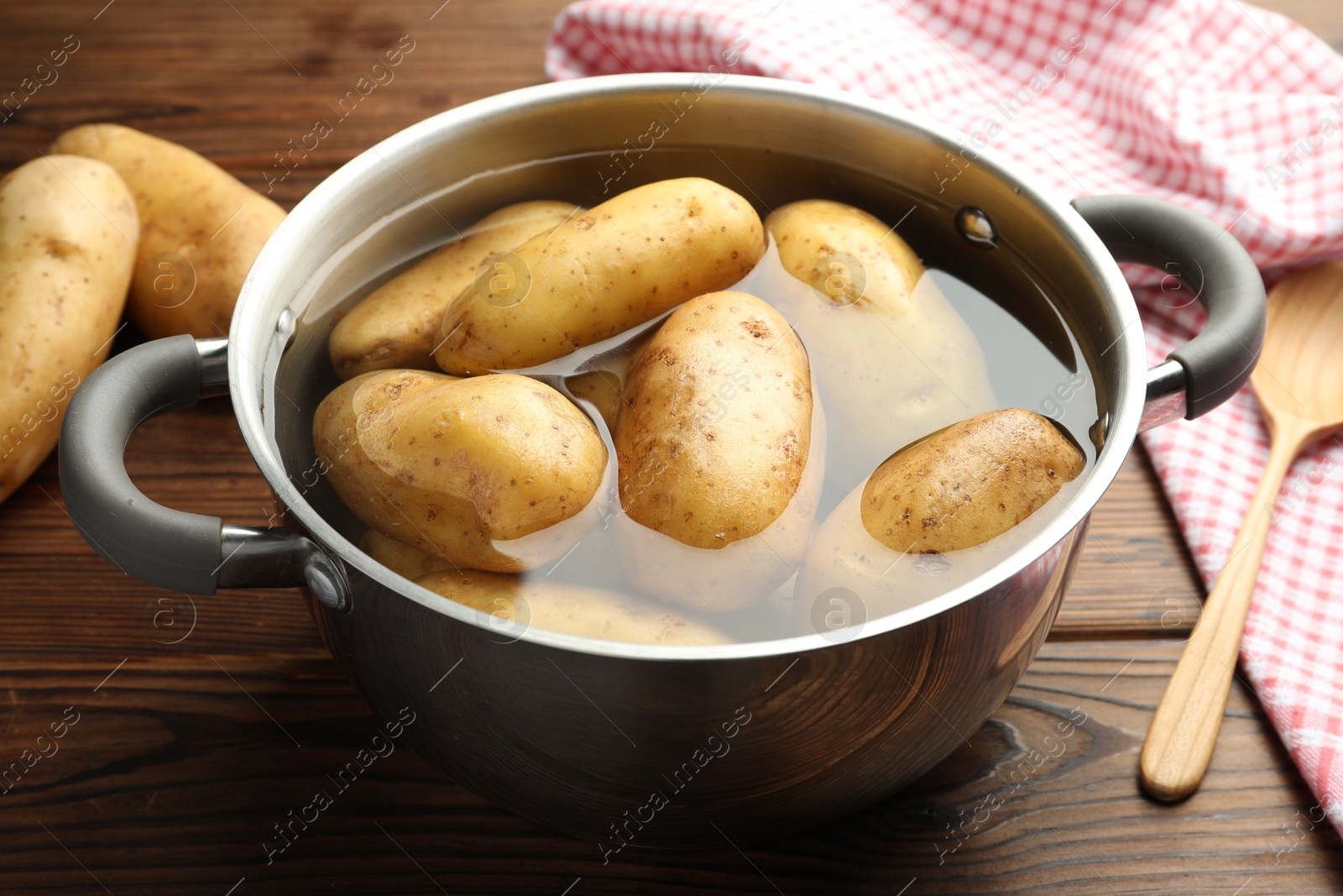 Photo of Raw potatoes in pot with water on wooden table