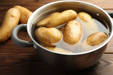 Photo of Raw potatoes in pot with water on wooden table, closeup