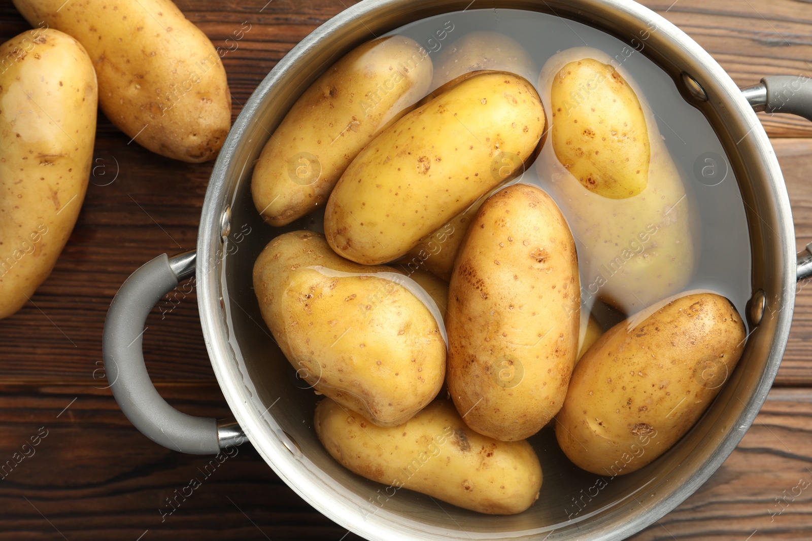 Photo of Raw potatoes in pot with water on wooden table, top view