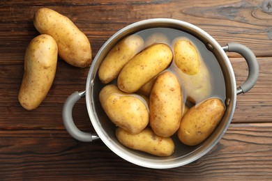 Raw potatoes in pot with water on wooden table, top view