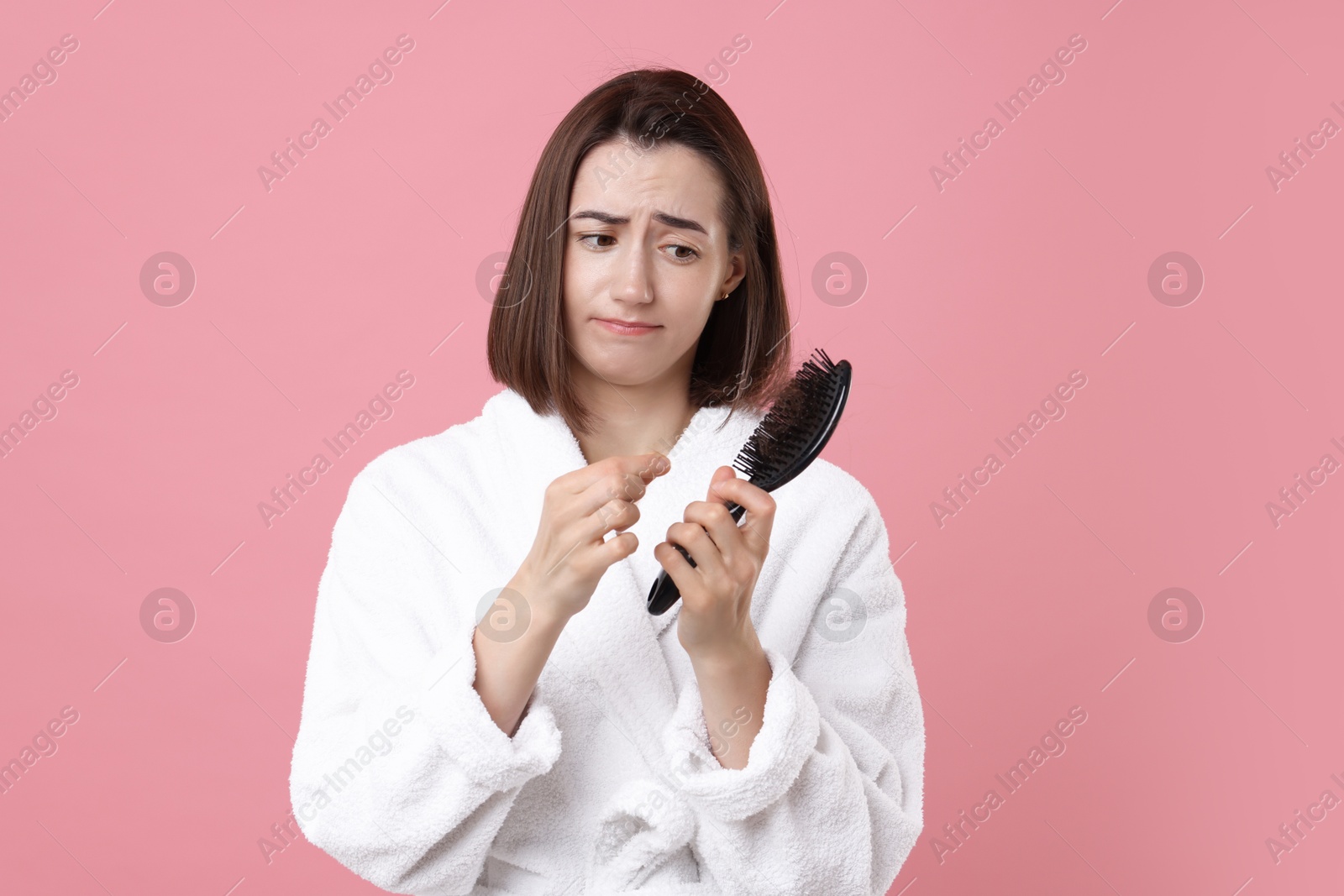 Photo of Sad woman holding brush with lost hair on pink background. Alopecia problem