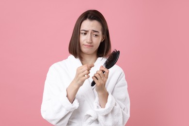 Photo of Sad woman holding brush with lost hair on pink background. Alopecia problem