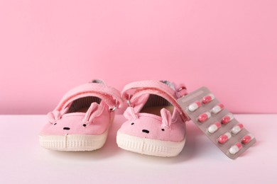 Cute baby shoes and pills on color background