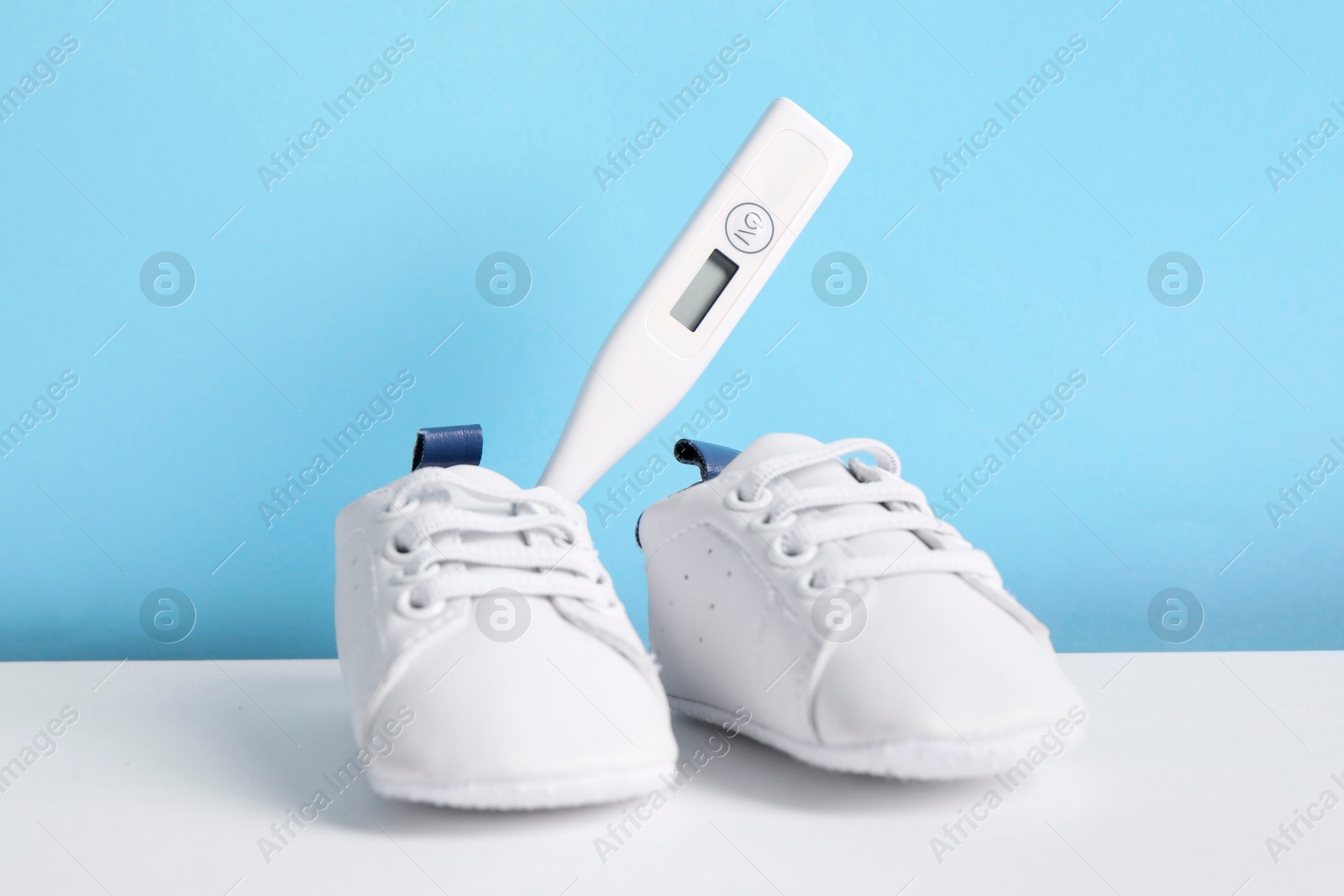 Photo of Child`s sneakers and thermometer on color background, closeup