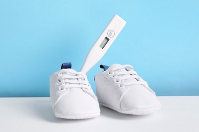 Child`s sneakers and thermometer on color background, closeup