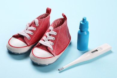 Kid's sneakers, thermometer and nasal spray on light blue background