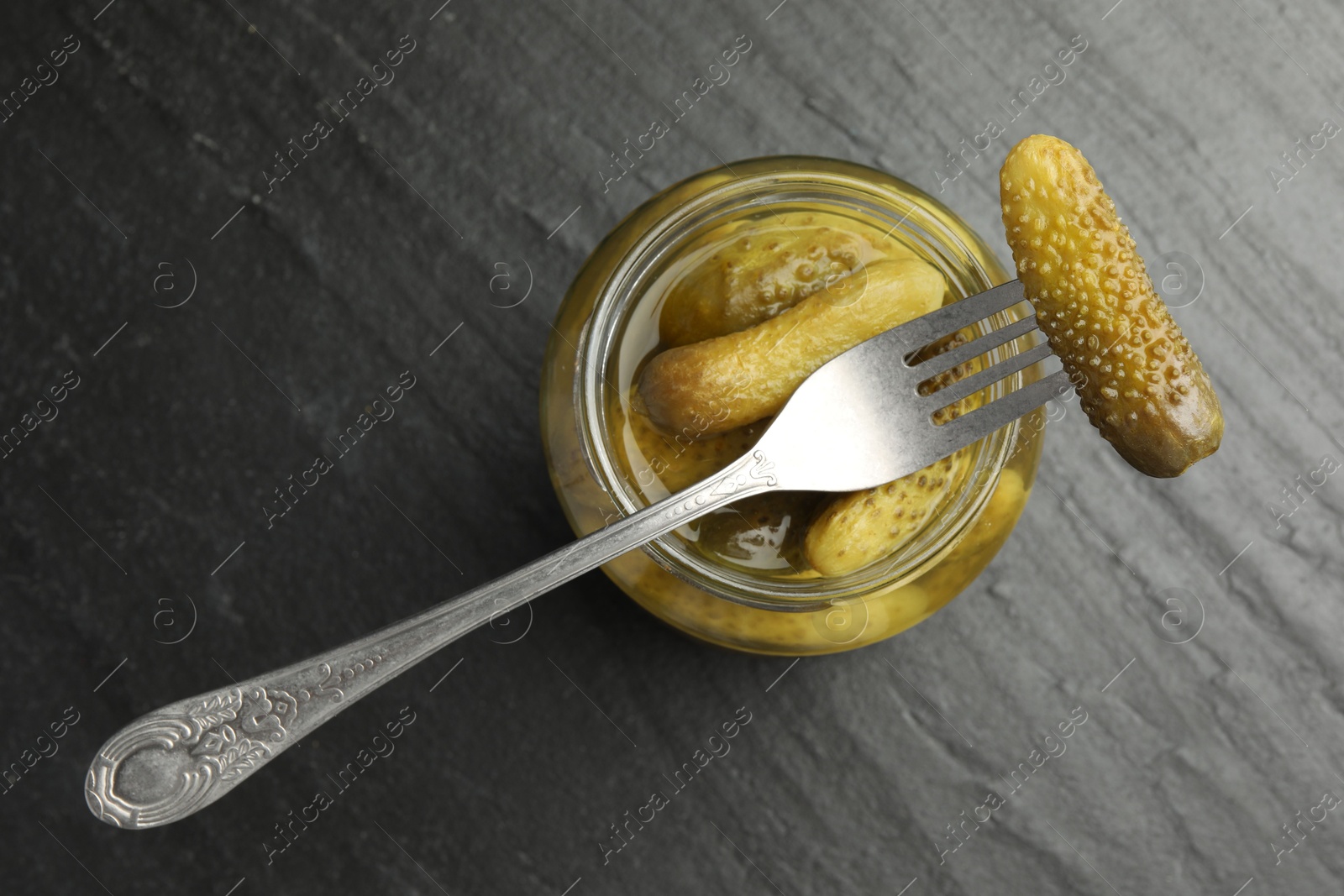 Photo of Fork with pickled cucumber on jar against grey background, top view