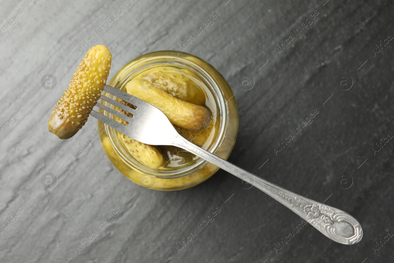 Photo of Fork with pickled cucumber on jar against grey background, top view