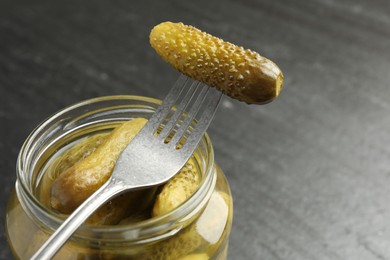 Photo of Fork with pickled cucumber on jar against grey background, closeup