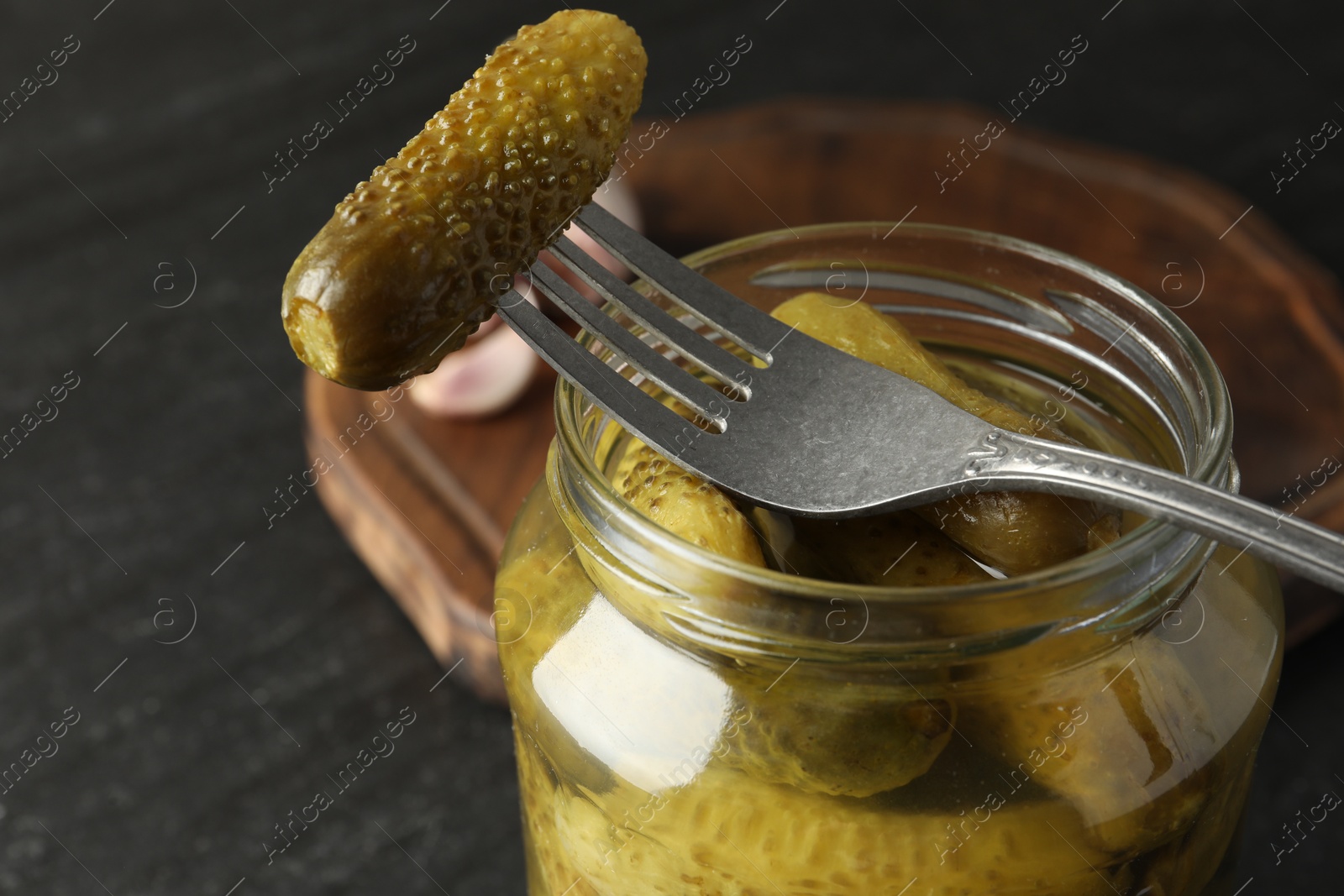 Photo of Fork with pickled cucumber on jar against grey background, closeup