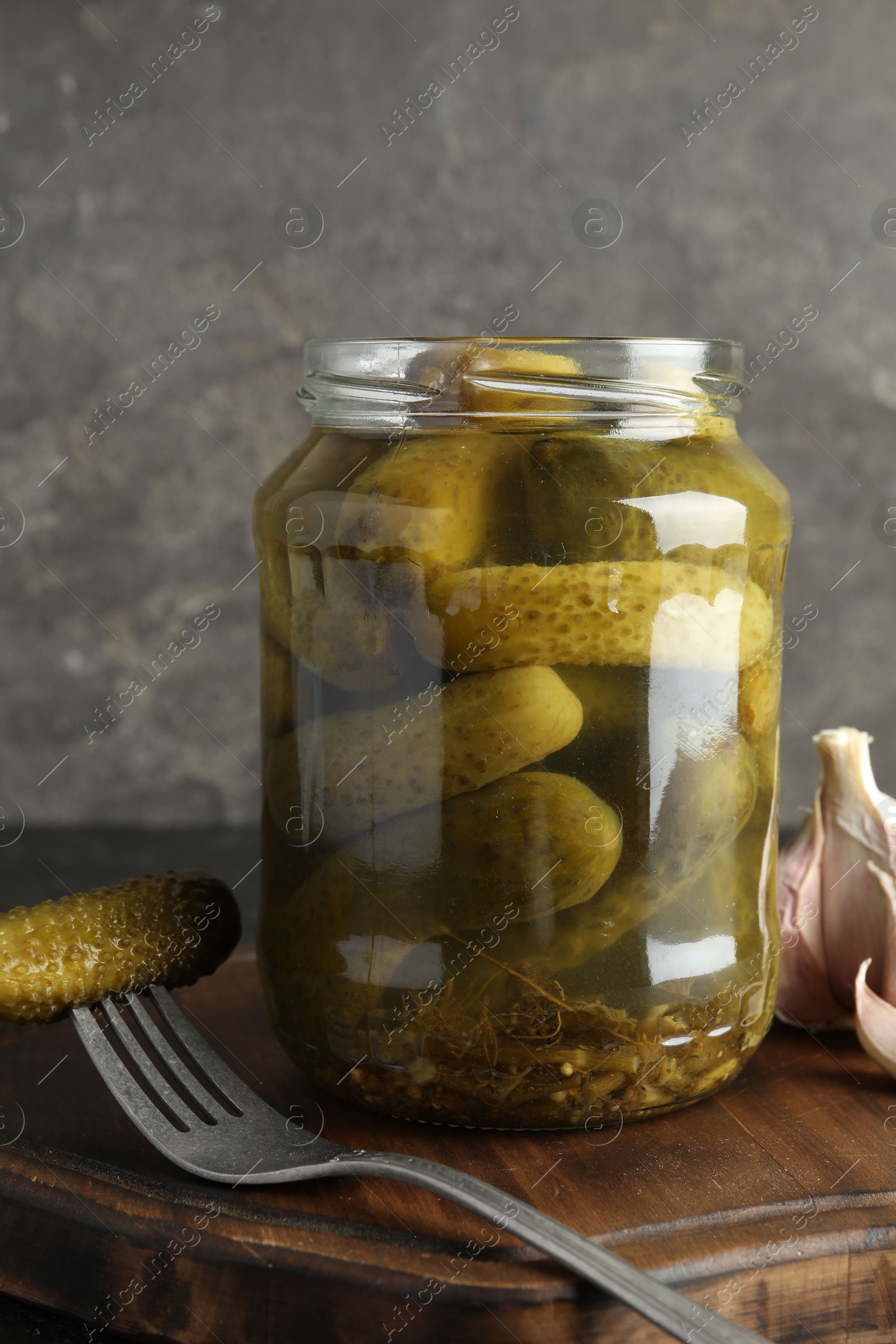 Photo of Pickled cucumbers in jar and garlic on table