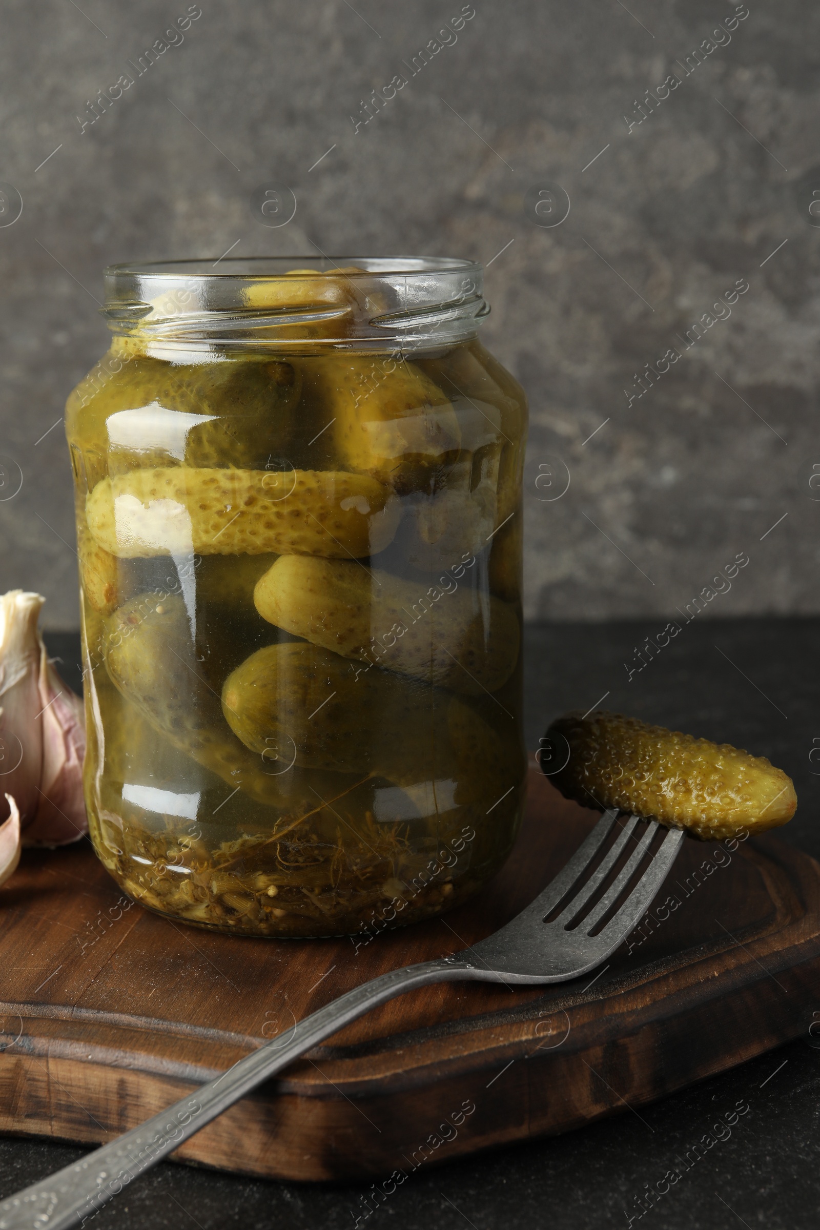 Photo of Pickled cucumbers in jar and garlic on grey table