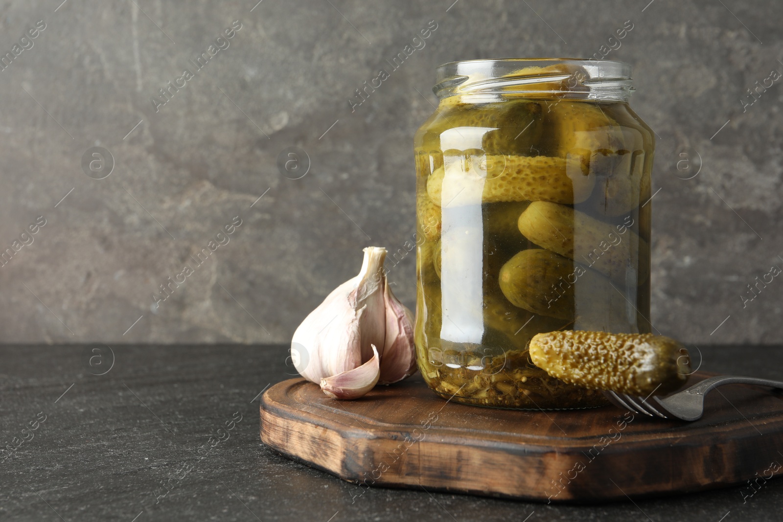 Photo of Pickled cucumbers in jar and garlic on grey table. Space for text