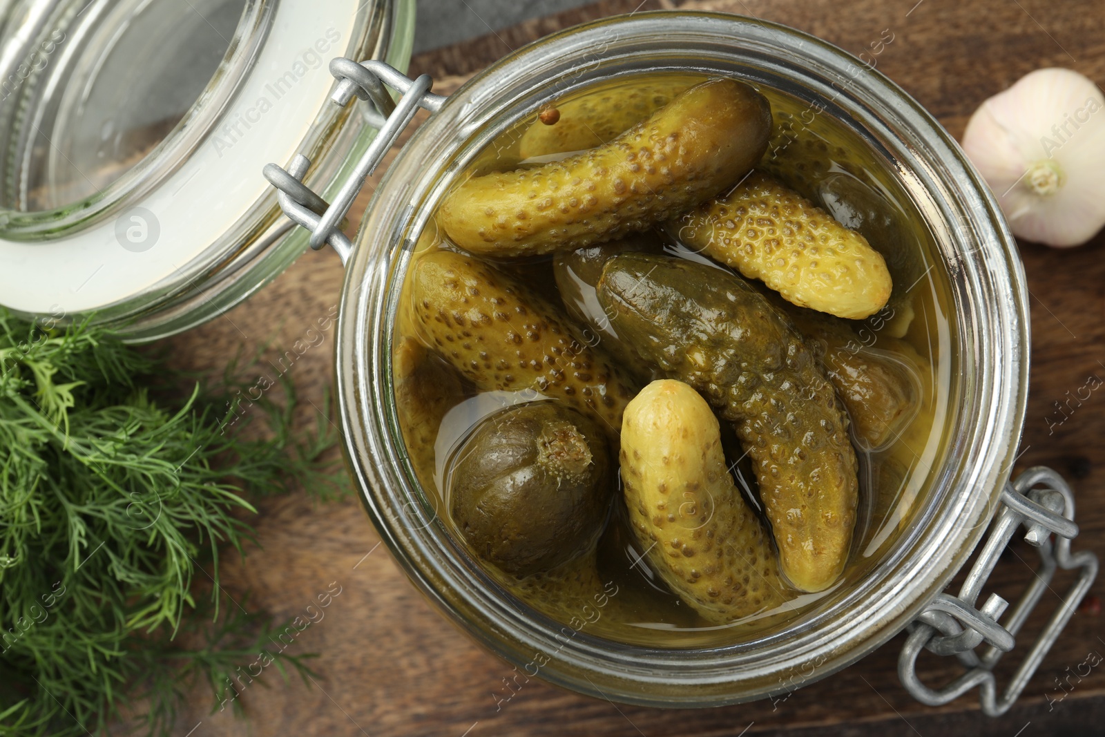 Photo of Pickled cucumbers in jar, garlic and dill on wooden table, flat lay