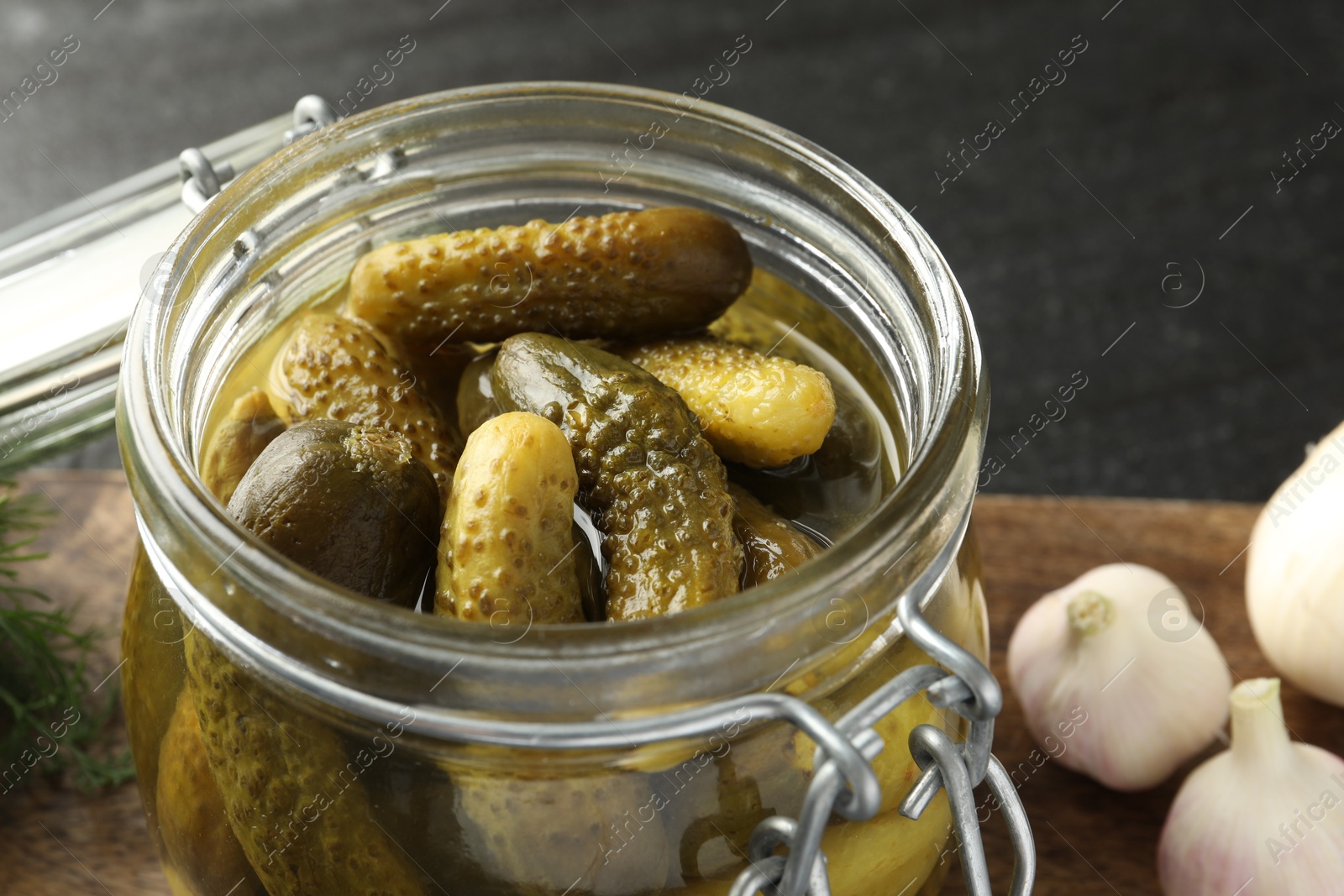 Photo of Pickled cucumbers in jar and garlic on grey table, closeup