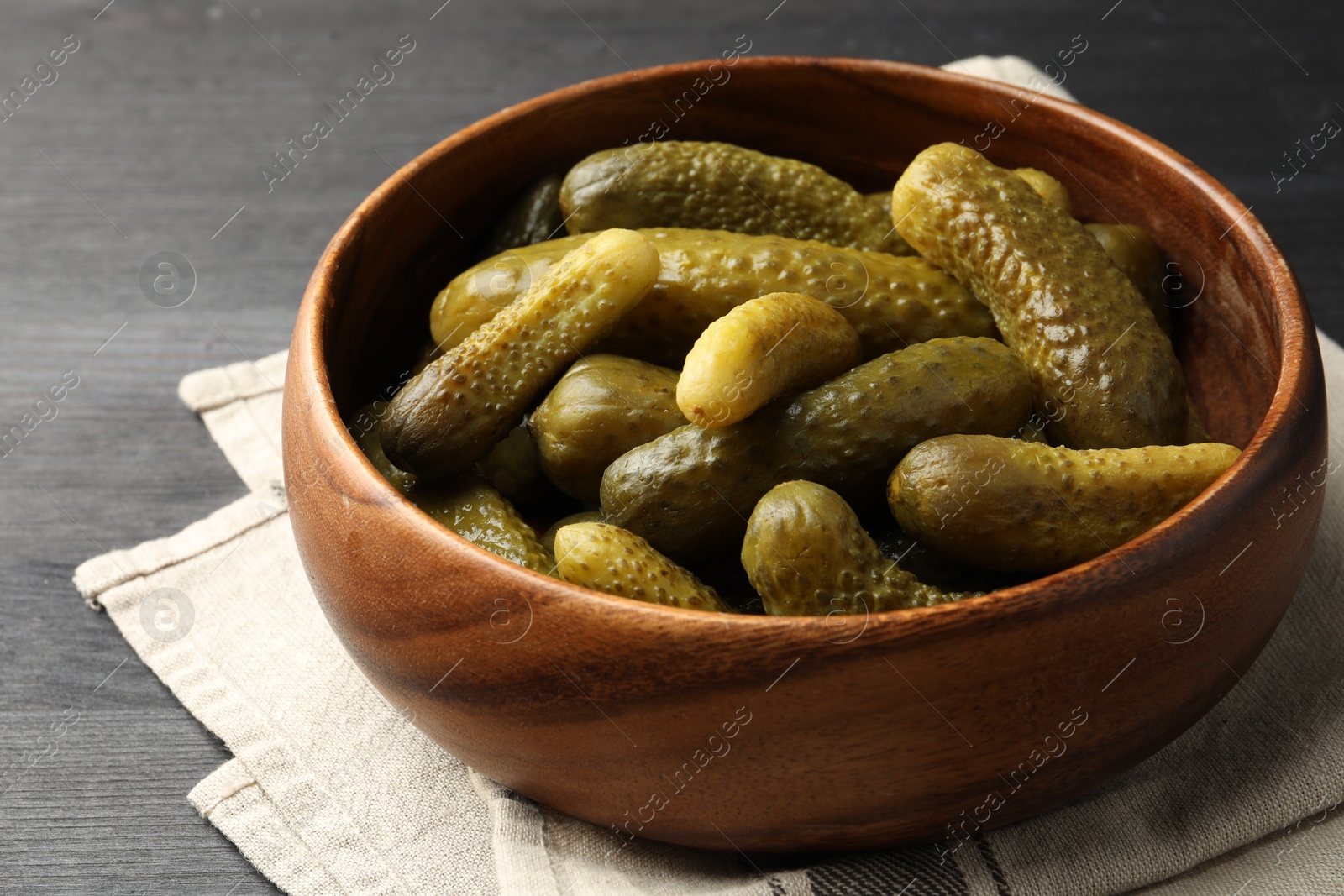 Photo of Pickled cucumbers in bowl on grey wooden table, closeup