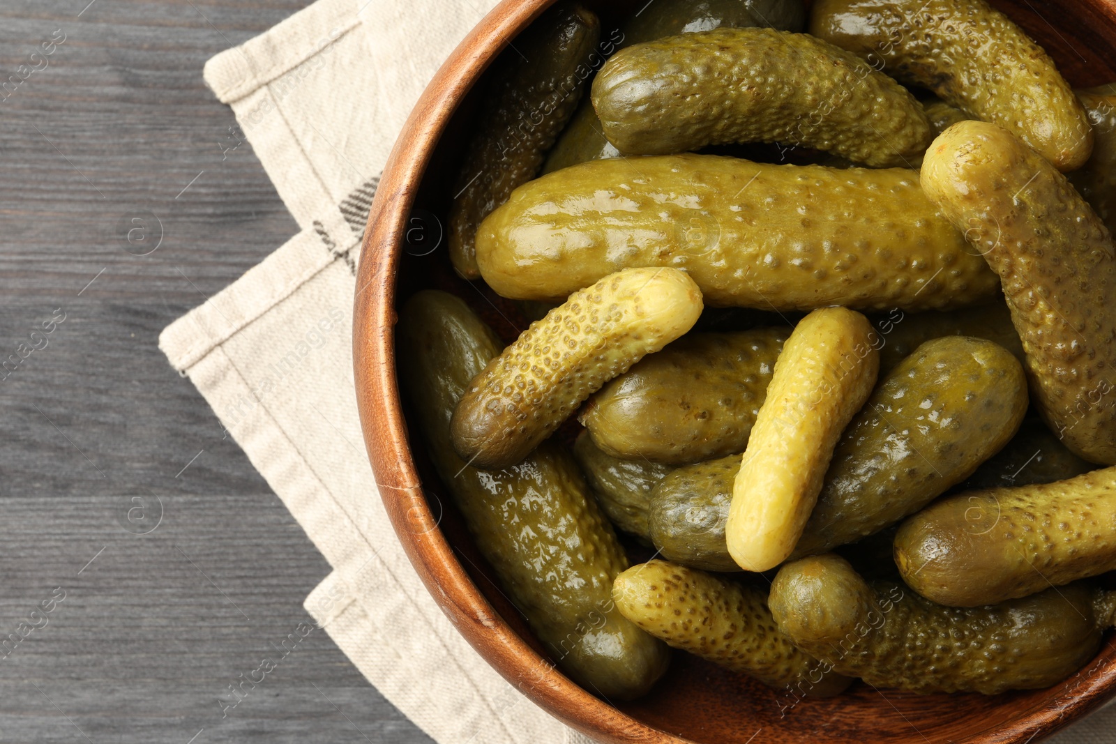 Photo of Pickled cucumbers in bowl on grey wooden table, top view