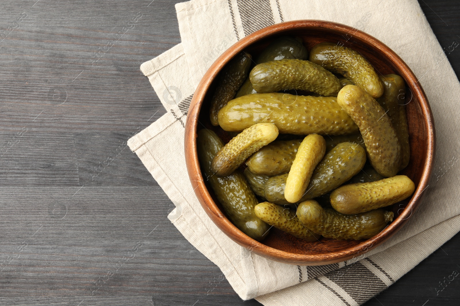 Photo of Pickled cucumbers in bowl on grey wooden table, top view