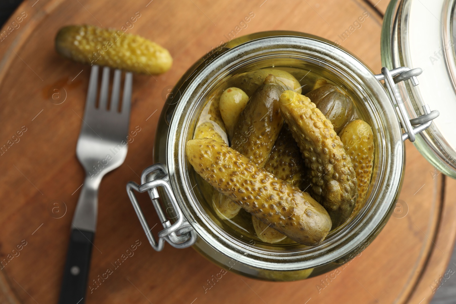 Photo of Pickled cucumbers in jar and fork on wooden table, top view