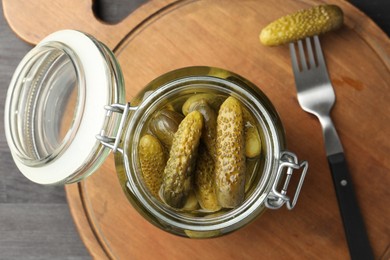 Photo of Pickled cucumbers in jar and fork on grey wooden table, top view
