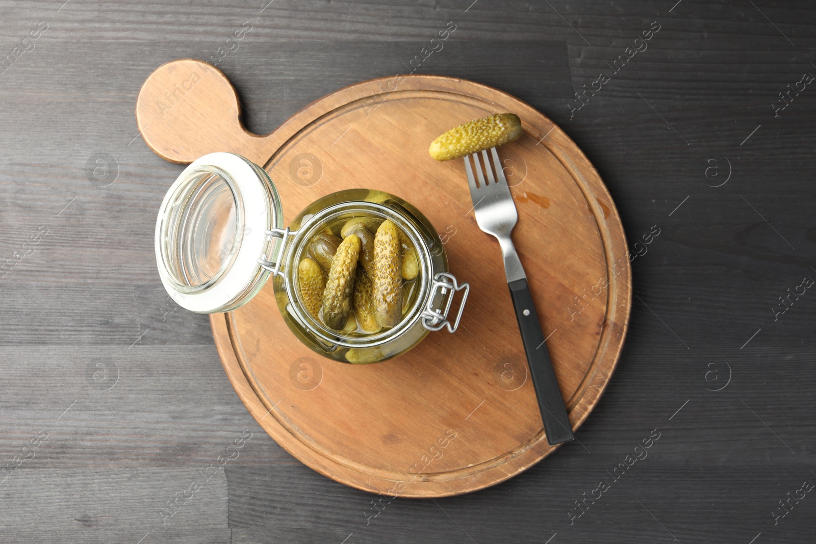 Photo of Pickled cucumbers in jar and fork on grey wooden table, top view