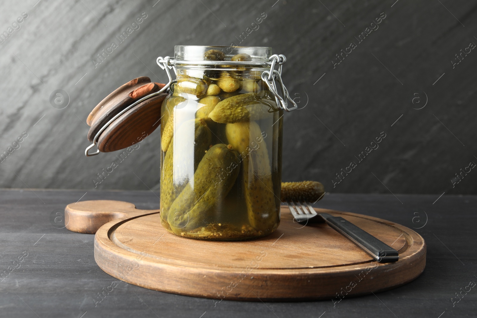 Photo of Pickled cucumbers in jar and fork on grey wooden table