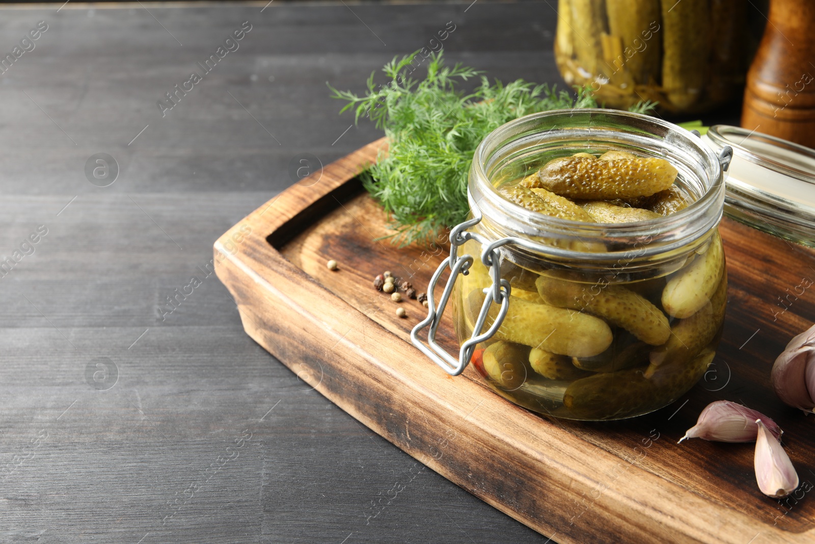 Photo of Pickled cucumbers in jar, garlic and dill on grey wooden table