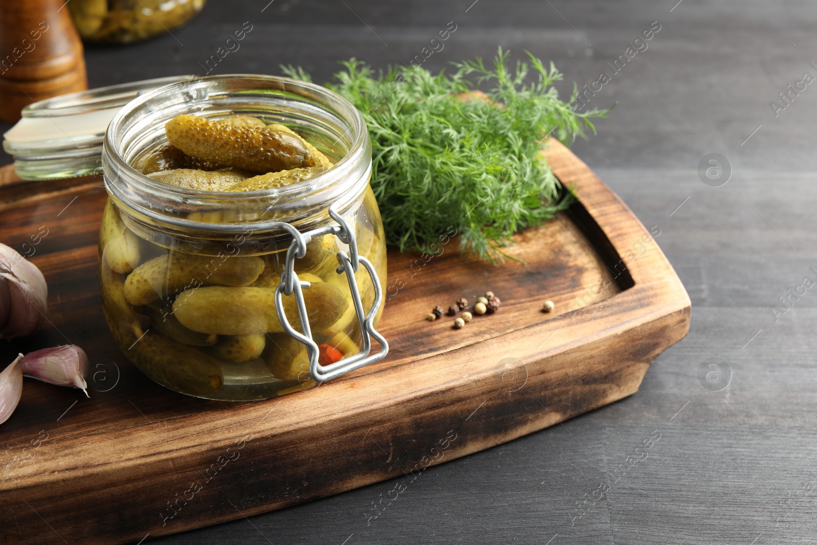 Photo of Pickled cucumbers in jar, garlic and dill on grey wooden table