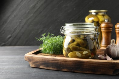 Photo of Pickled cucumbers in jars, garlic and dill on grey wooden table