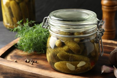 Photo of Pickled cucumbers in jars, garlic and dill on grey wooden table, closeup